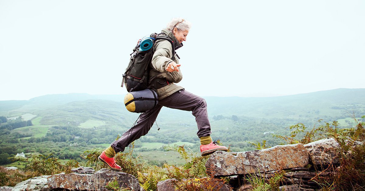 A woman climbing over rocks with a backpack on her shoulders.