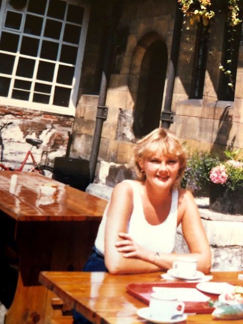 A blonde 35-year-old woman sitting at an outdoor restaurant in Europe on her first post-divorce solo journey