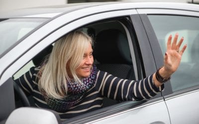 A smiling woman waving out of her car window