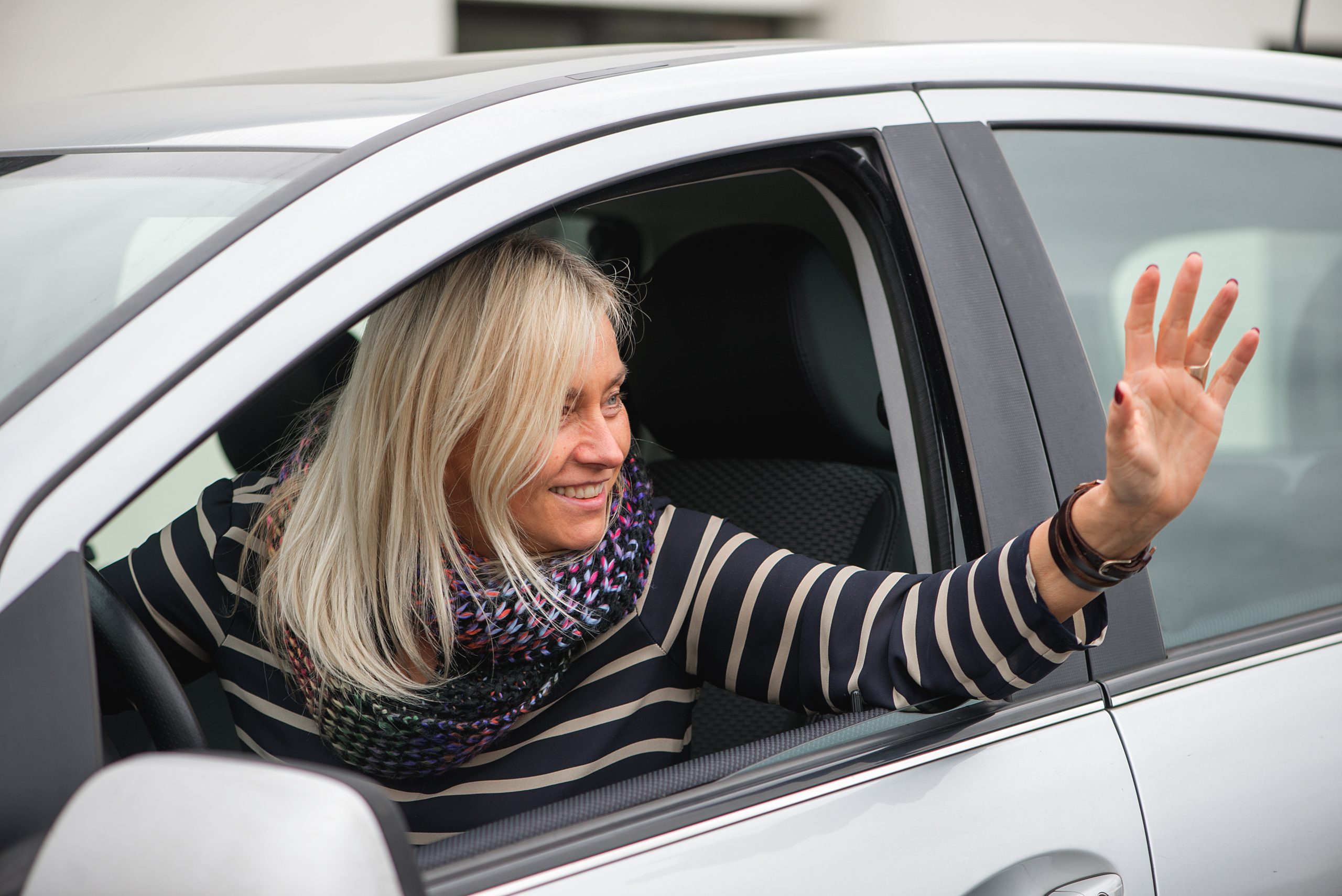 A smiling woman waving out of her car window