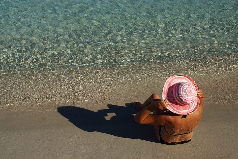 Mature woman in bikini and sun hat sits on a beach