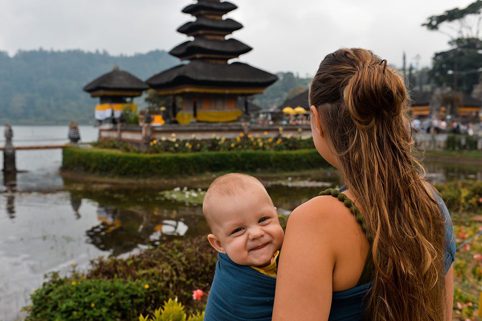 Young baby being worn by mother smiles for the camera in Bali