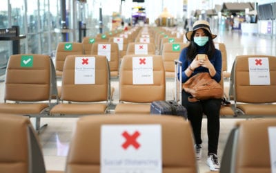 Young woman sits alone in airport at gate wearking mask and social distancing