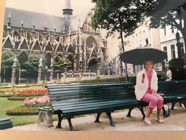 Marillee sits on a park bench under an umbrella