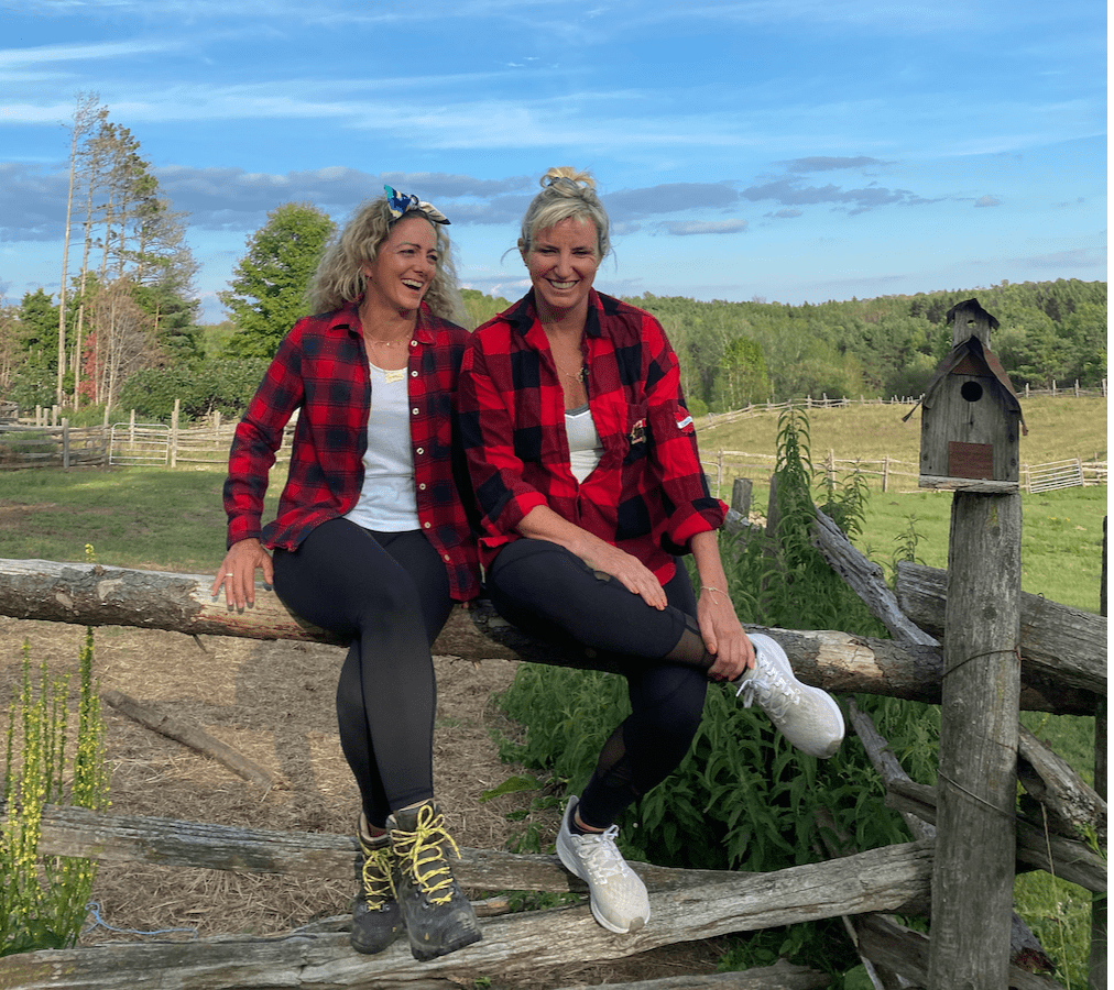 Two women sitting in flannel in front of a trail.