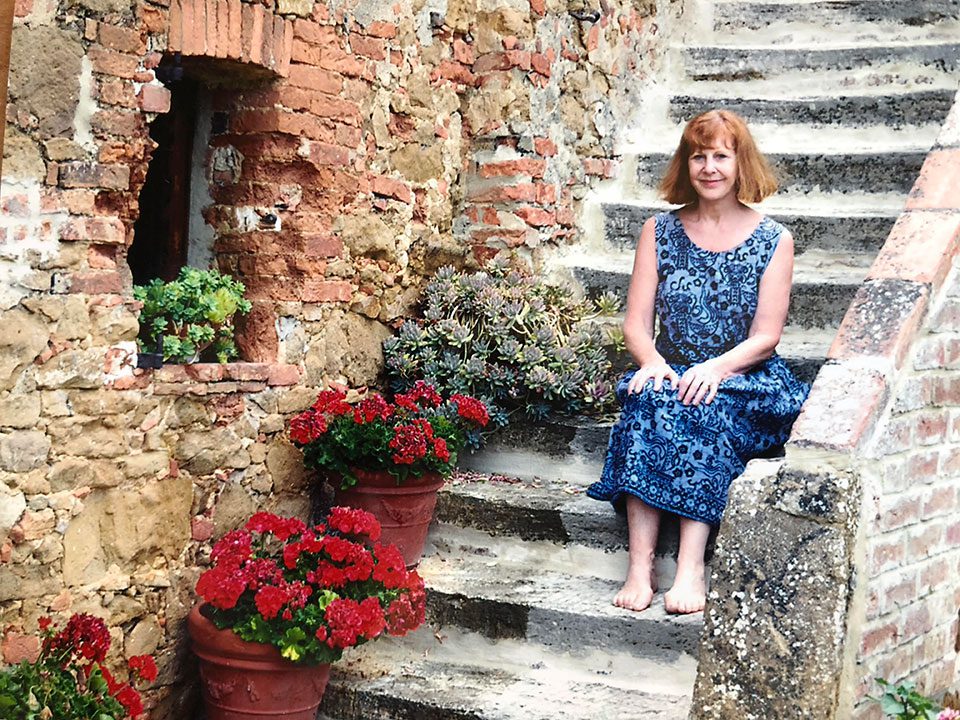 The author sits in a blue dress on the stone steps of her Italian villa