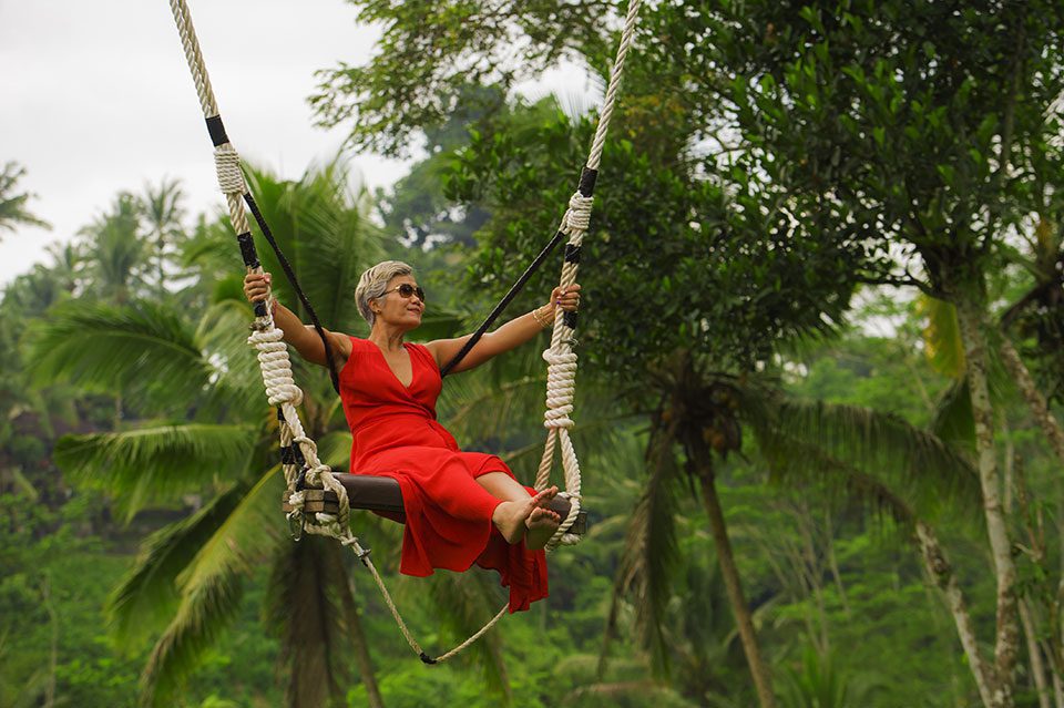 Smiling woman in bright red dress on tree swing