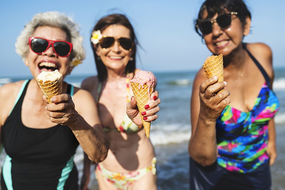 Three mature women enjoying ice cream on beach