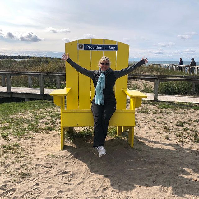 Carolyn stands before big yellow Muskoka Chair on Providence Beach