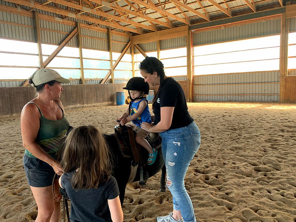 Little boy rides a miniature pony with mother and teacher to help