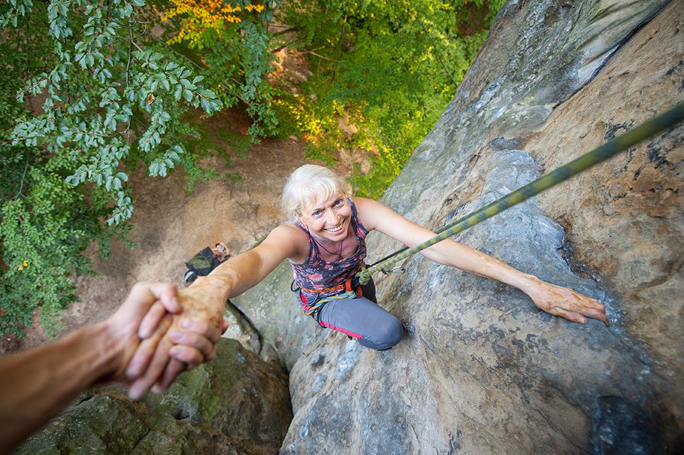 Older woman rock climbing smiles up at camera