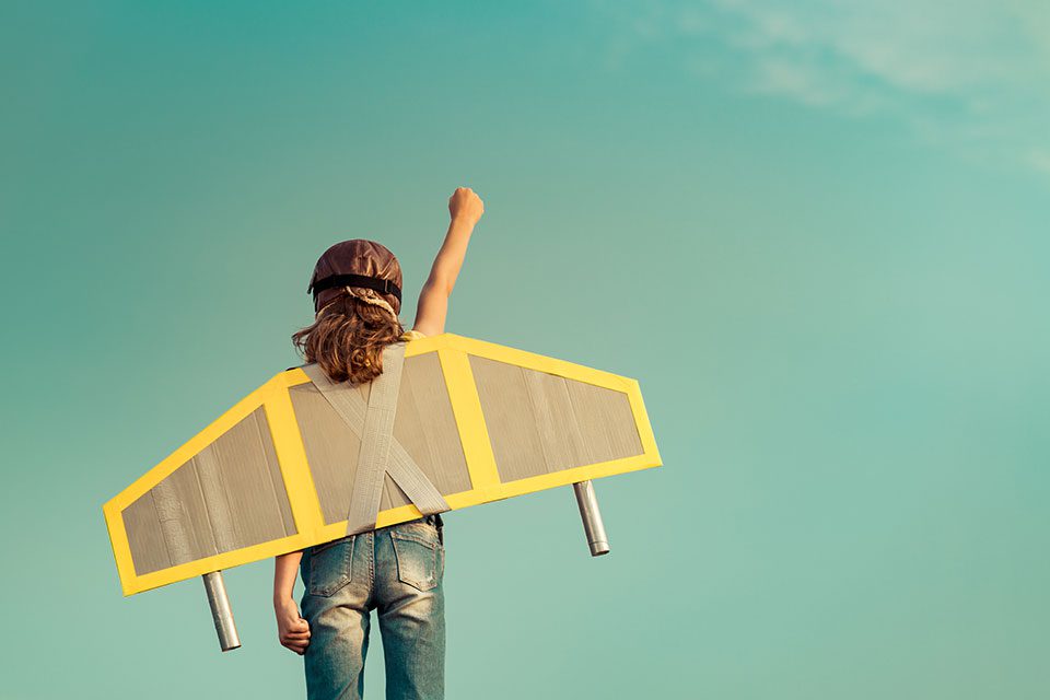 Young girl pretends to fly with cardboard plane wings