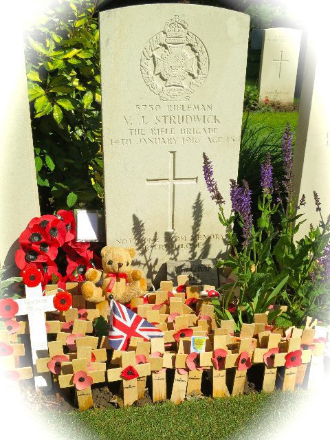 A grave stone surrounded by handmade crosses and poppies