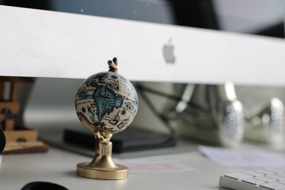 A small globe on top of a table in front of a computer monitor