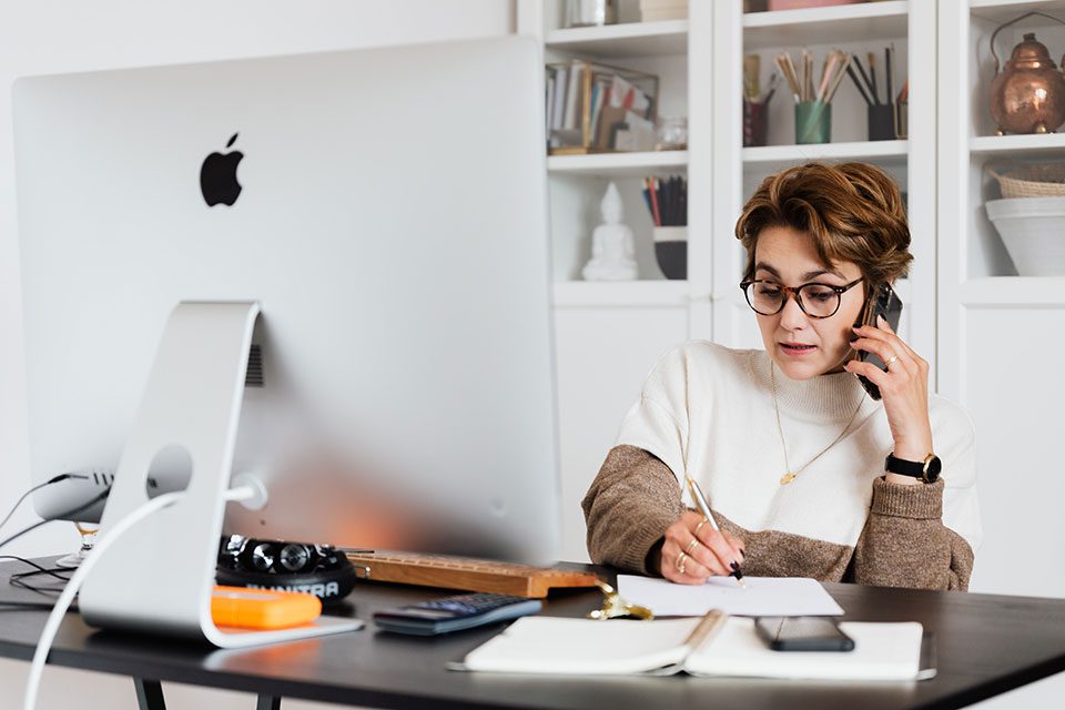 Mature woman sitting at a computer and talking on the phone