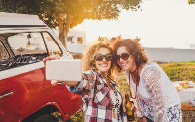 Two adult woman taking a picture beside red rv while travelling