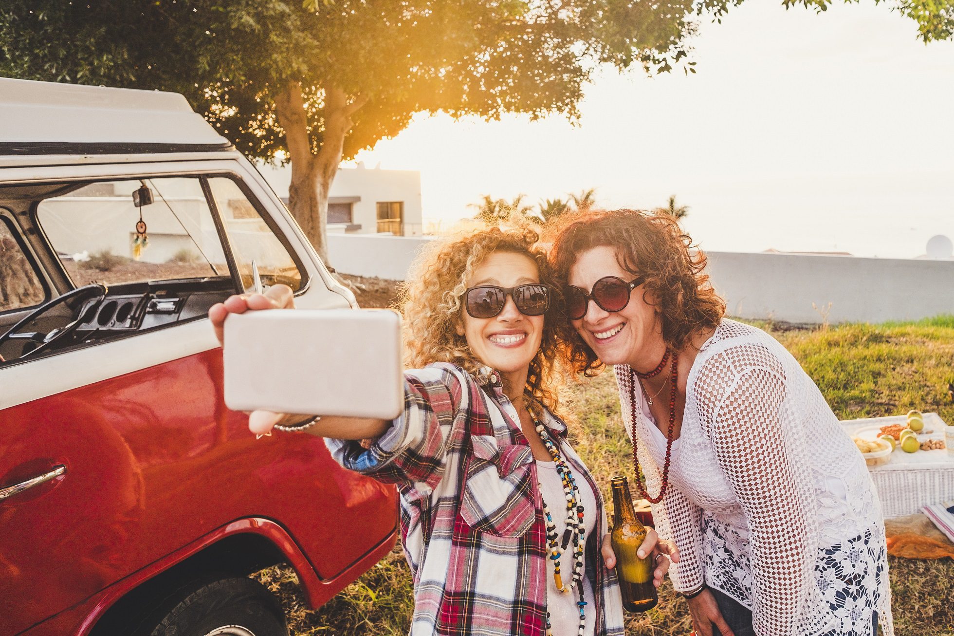 Two adult woman taking a picture beside red rv while travelling