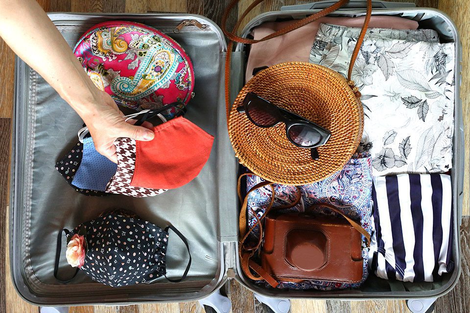 Flat lay, woman packing suitcase with face masks