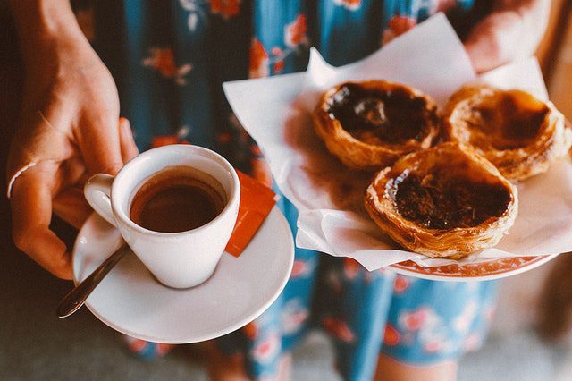 Woman holds a cup of coffee and plate of pasteries