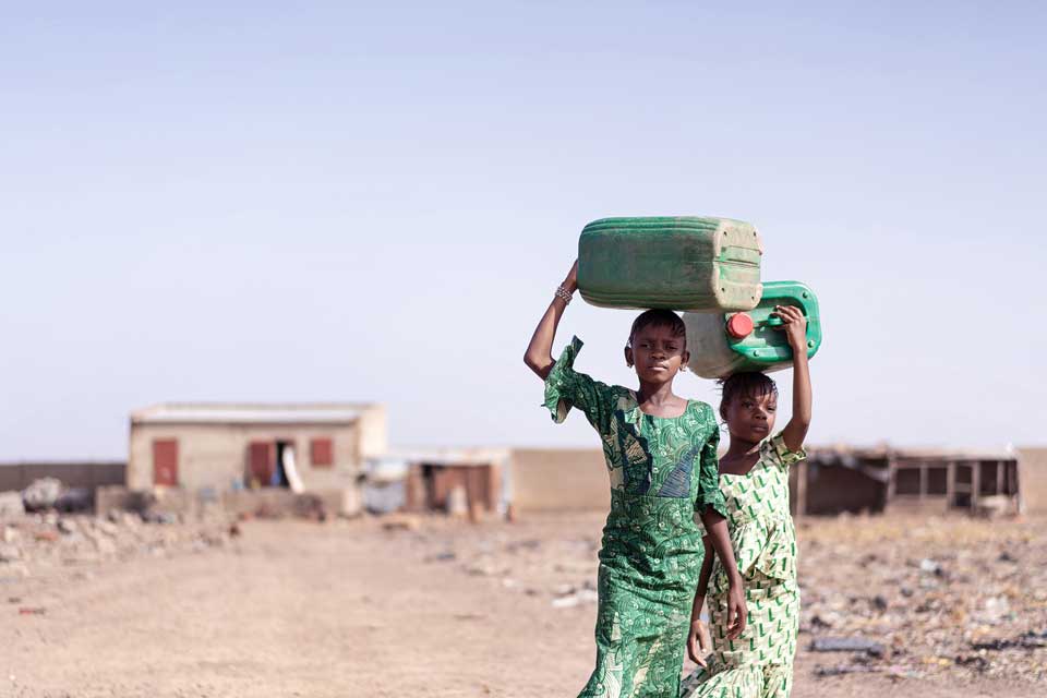 Two young women carry water jugs, Zimbabwe