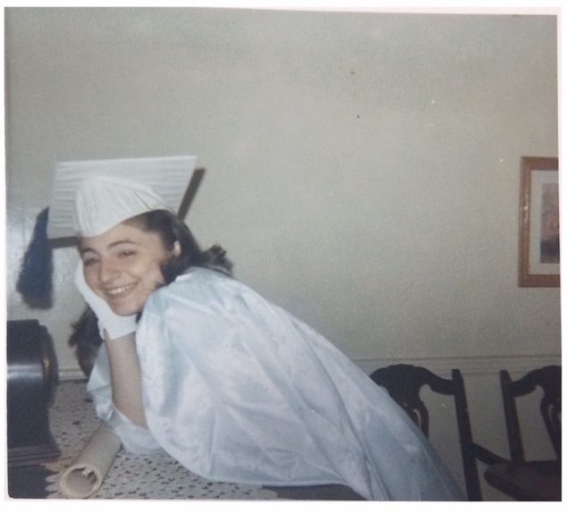 A woman wearing a white graduation gown and cap.