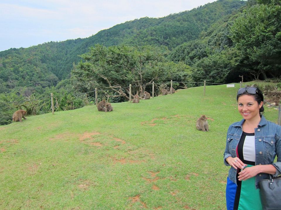 A woman standing on a field with monkeys in the background.