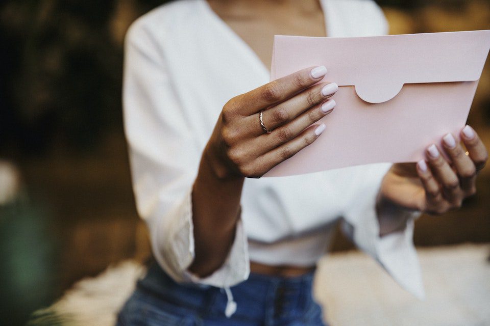 A woman holding a pink envelope, reading a love letter from her older self.