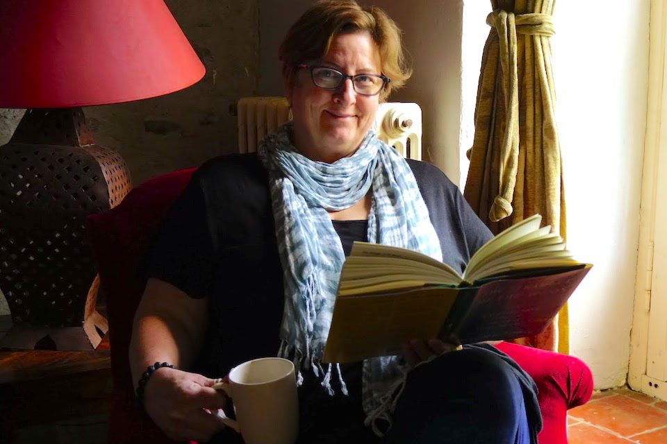 A woman sitting in a chair reading a book. Learn about solo travel for women over 50