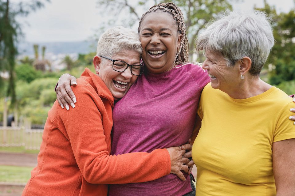 Three older women embracing and smiling, sharing their travel wisdom for the ages.