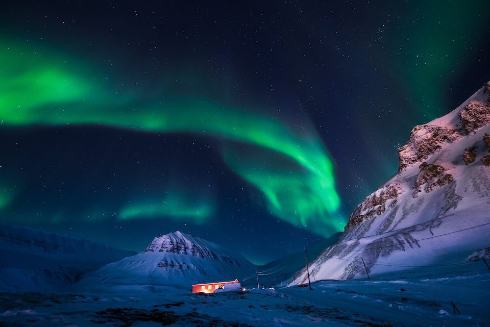 The Northern Lights dance around lit up cabins in Svalbard, Norway