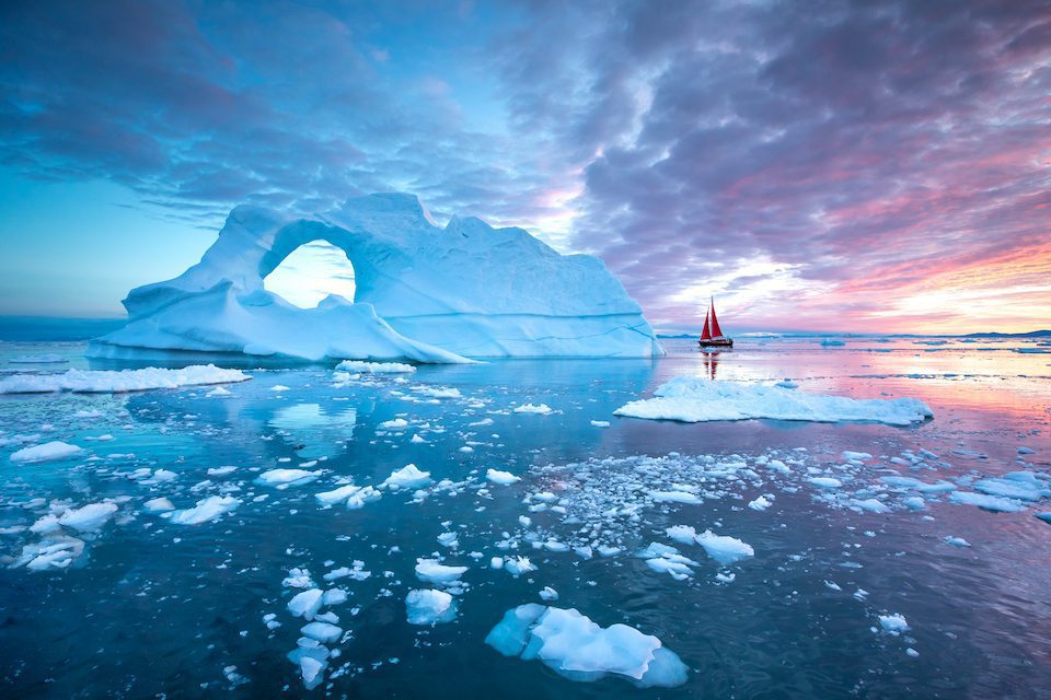 A sailboat floating past icebergs in Disko Bay, Greenland, one of our off the beaten path destinations.