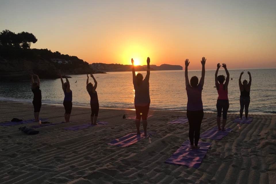 A group of women doing yoga on the beach at sunset