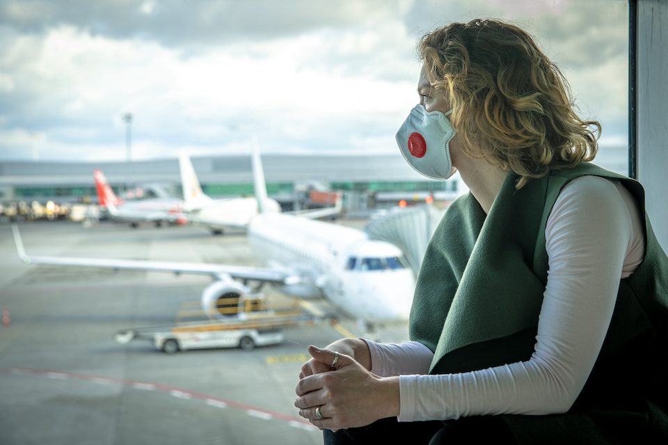A woman sitting at an airport with a mask on her face. Here are our top travel tips for women in June 2021.