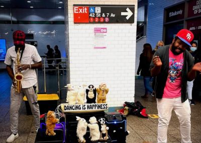 Two buskers performing in a New York City subway station, one dancing and one playing the saxophone.