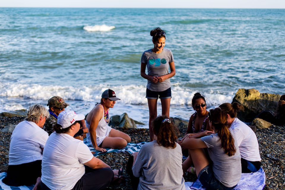 A group of women sit in a circle next to the sea during a transformative travel experience