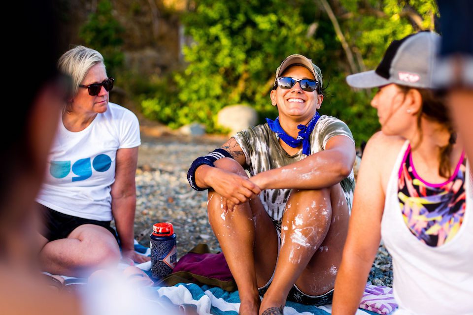 A group of women sitting on a beach and talking, wearing white tshirts part of a transformative travel experience