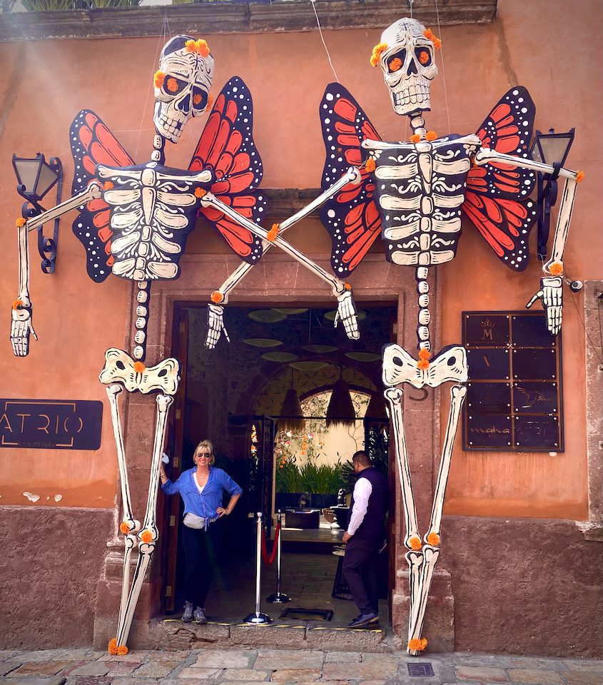 Carolyn standing with two skeleton statues with butterfly wings in San Miguel de Allende