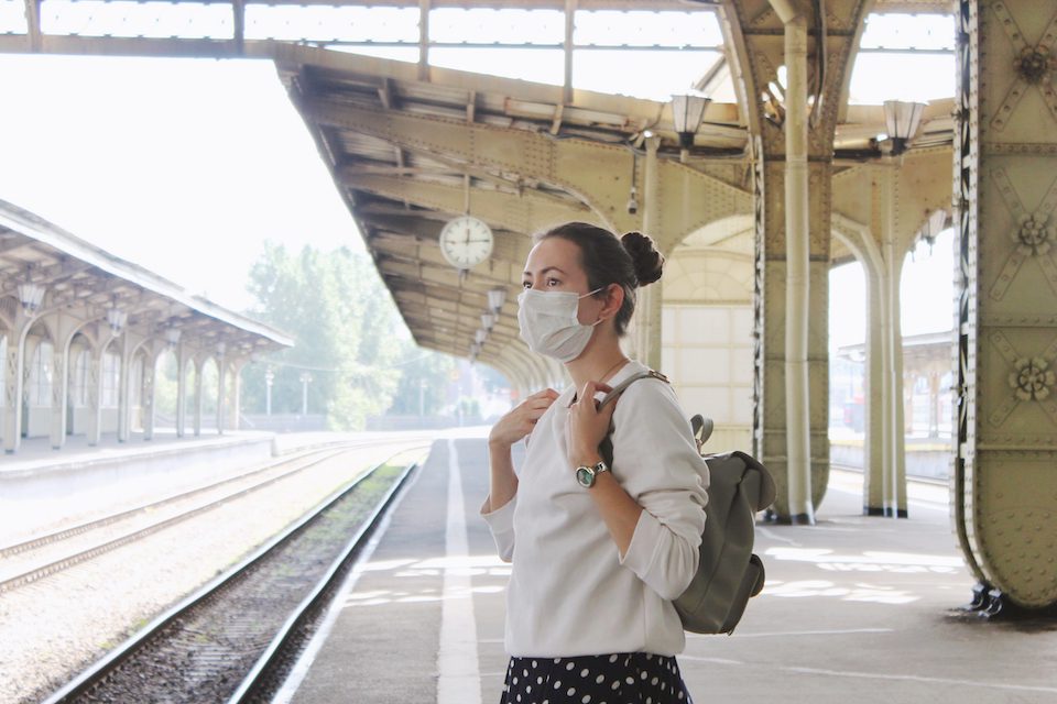 A woman wearing protective face medical mask is waiting for the train at the railway station