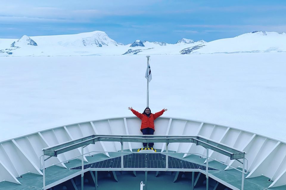 A woman at the front of a boat over ice in Antarctica