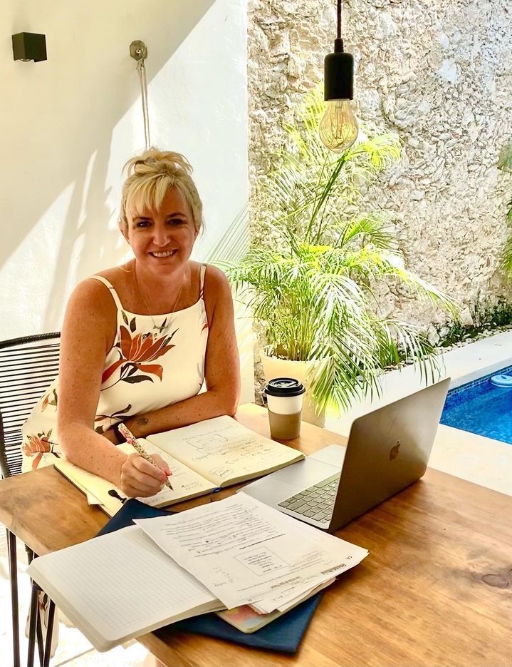 A woman works at a table beside a pool in a homestay in Mexico