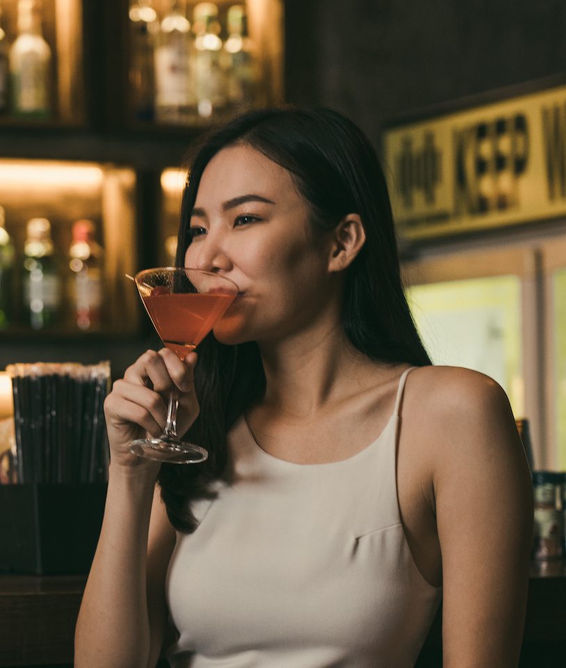 woman drinking a cocktail at a bar at night.
