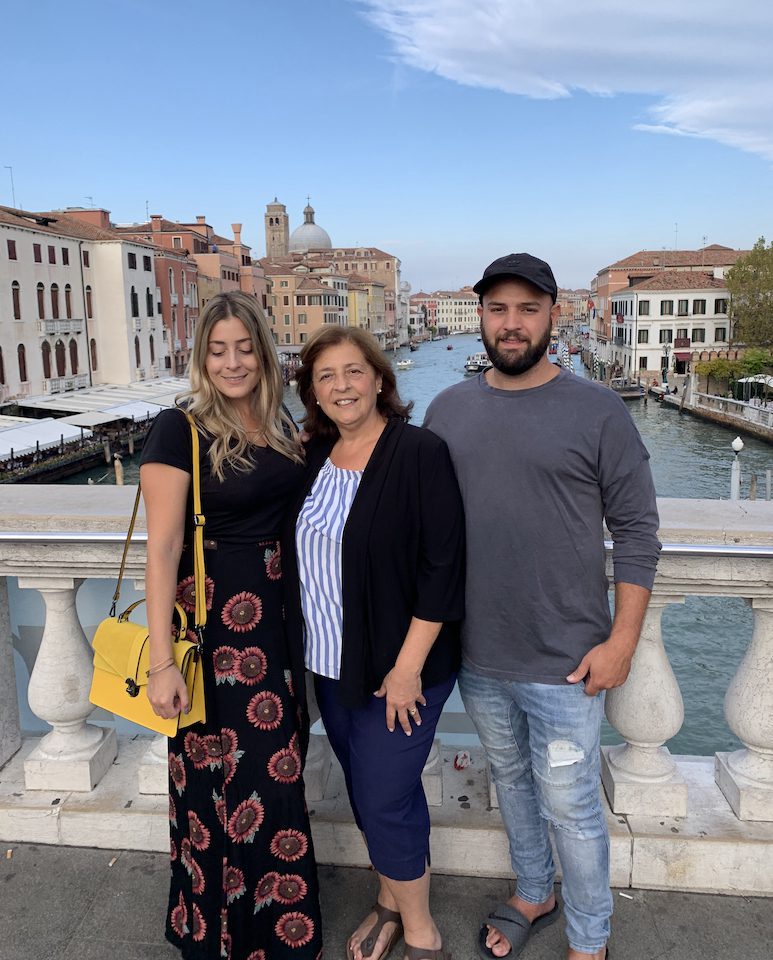 Three people stand on a bridge over a canal in Venice