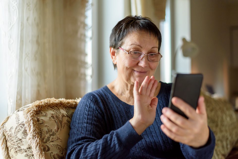 Senior woman in eyeglasses making video call on smartphone at home