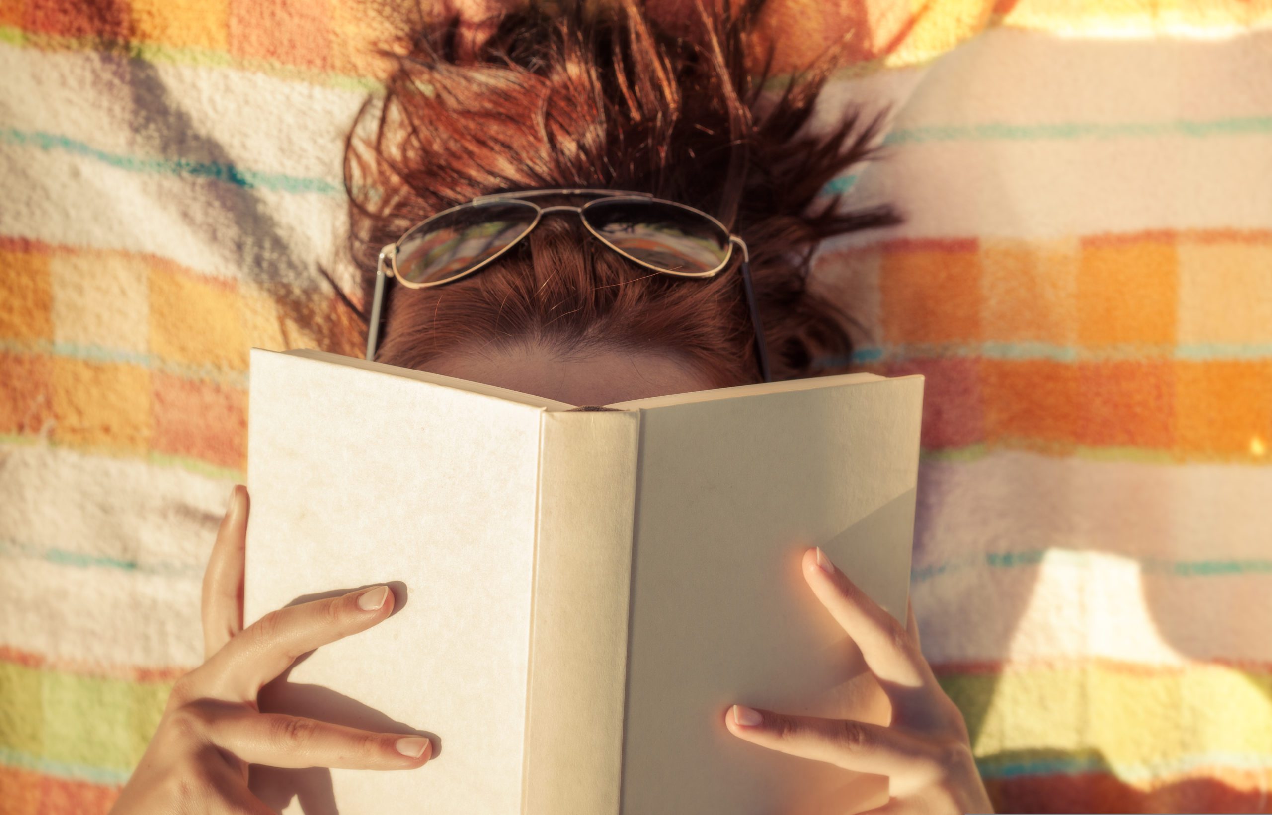A woman lays holding a book over her head