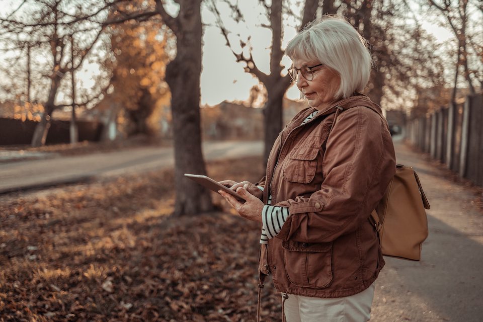 An older woman uses a tablet while out for a walk