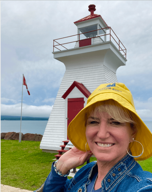 Carolyn wears a yellow hat in front of a Nova Scotia Lighthouse