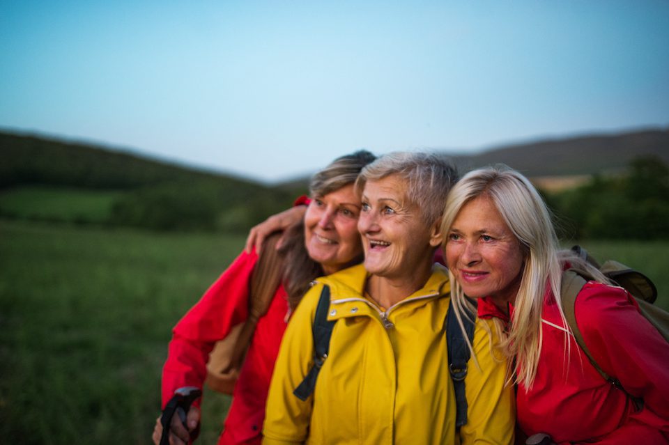 Happy senior women friends on walk outdoors in nature at dusk.