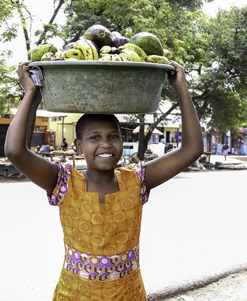 A girl carries a basket of fruit on her head in Tanzania
