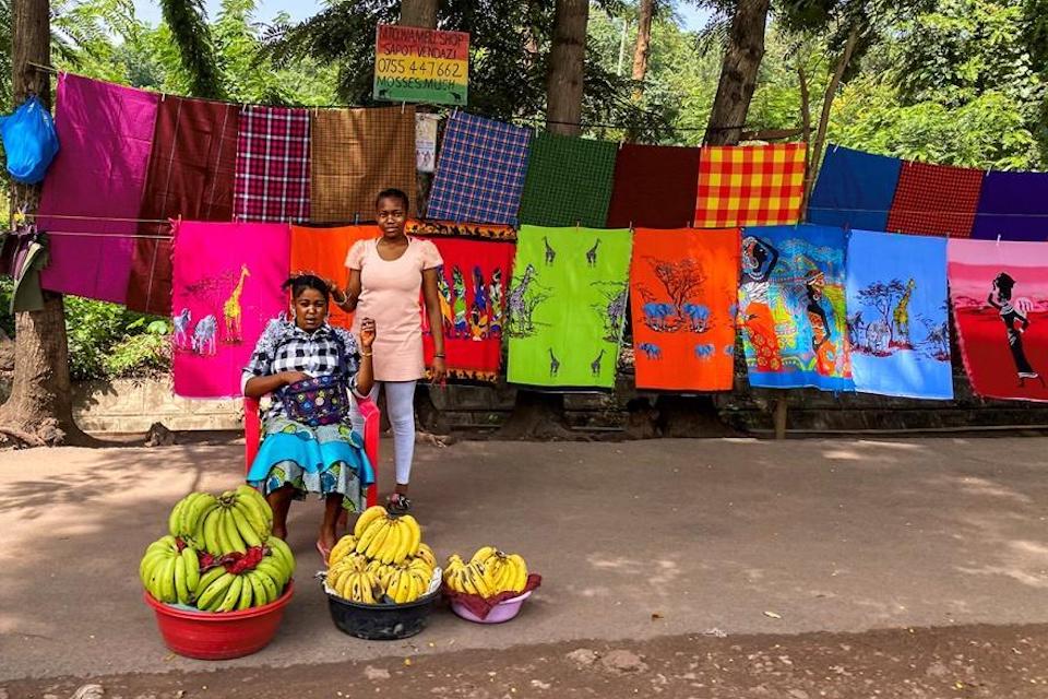 Two women sell fruit and other goods at an outdoor shop in Tanzania