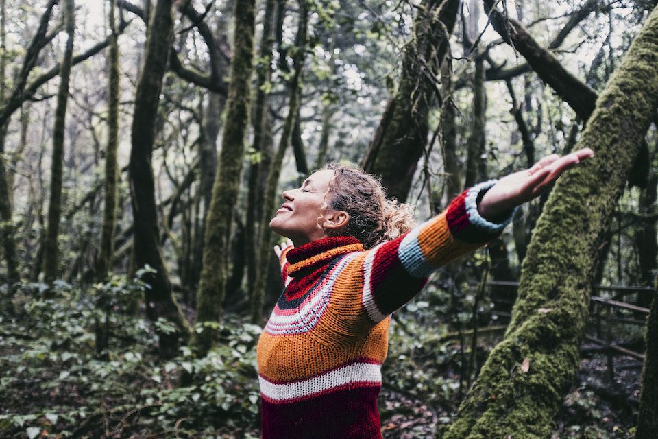 Happy adult woman smile and open arms to embrace beautiful nature forest around her.